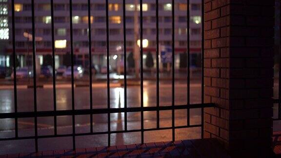 雨夜潮湿的城市街道透过金属栅栏的夜间交通画面