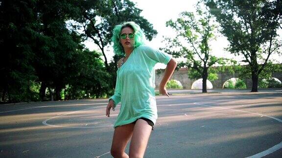 年轻时髦的女孩带着绿色的头发和太阳眼镜在户外跳舞慢镜头
