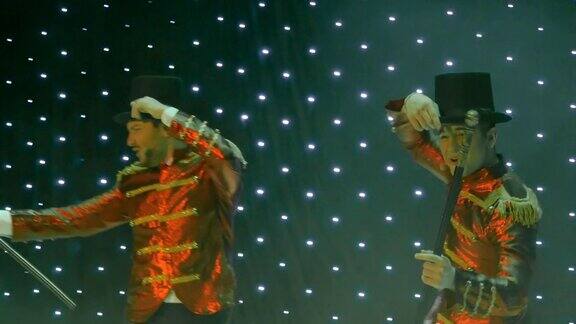 两个穿着红色燕尾服的时髦男子正在剧院的舞台上载歌载舞