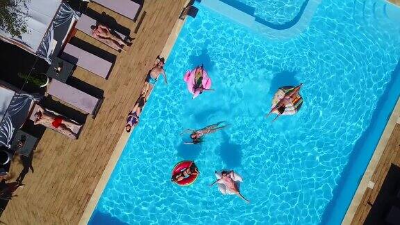 天线朋友们在游泳池和充气火烈鸟天鹅床垫快乐的年轻人在豪华度假村的漂浮床垫上沐浴从以上观点穿着比基尼的女孩在阳光下晒太阳