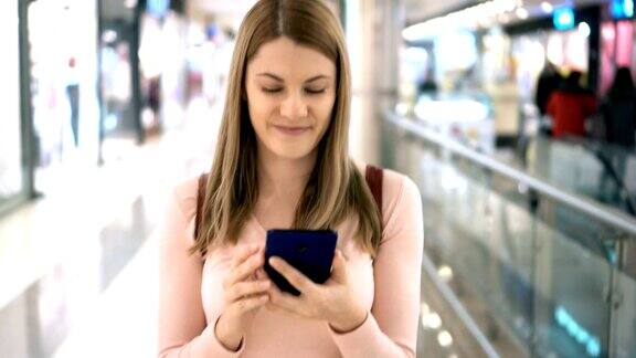 漂亮女人拿着智能手机在商场里走浏览互联网与朋友交流