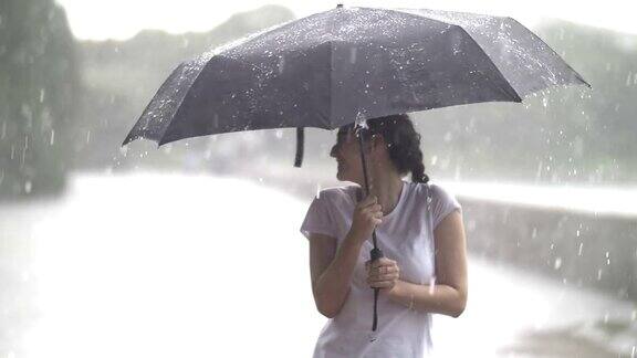 快乐的女孩在伞下享受着雨下着大雨慢动作在户外