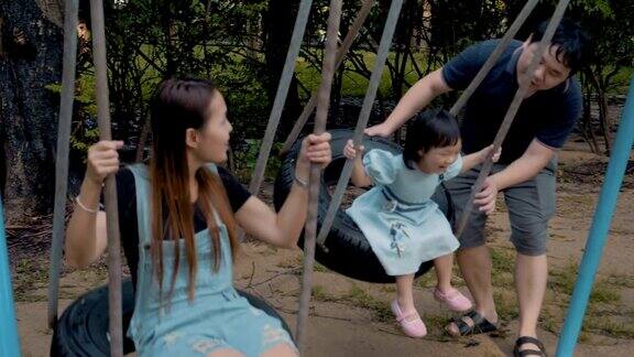 亚洲家庭与一个小女孩荡秋千享受在公共公园