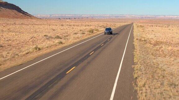 空中的黑色越野车在旅途中驾驶在空旷的道路上通过广阔的沙漠山谷