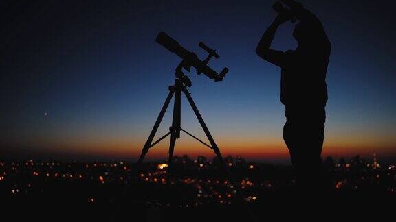一个人、望远镜和星空下的乡村的剪影