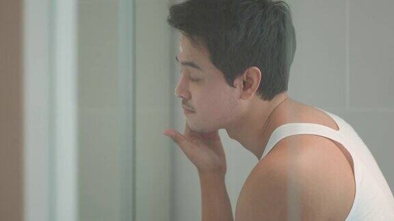 一名亚洲男子在洗澡后往脸上涂抹保湿面霜准备在家里的浴室里工作