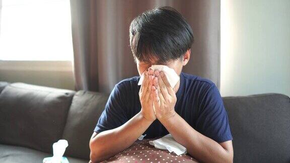 一个坐在客厅沙发上捂着纸巾打喷嚏的亚洲男人