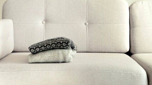 女人把暖和的毛衣堆在灰色舒适的沙发上