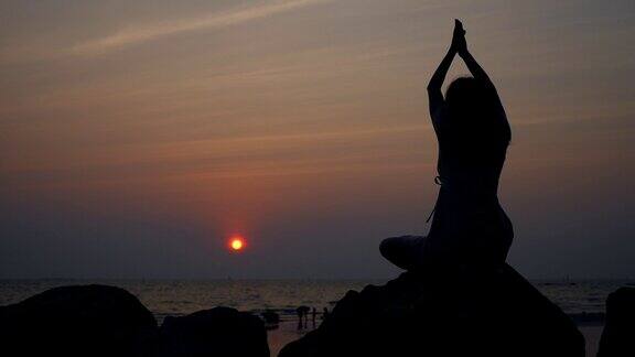 日落时分女孩在海滩上练习瑜伽的剪影场景