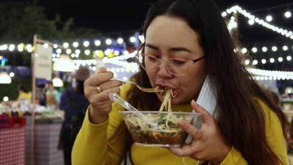 4K亚洲女孩吃泰国街头食物叫yum米粉木托盘在夜市的人走