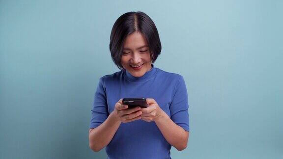 一名快乐的亚洲女性在蓝色背景下使用智能手机4k的视频