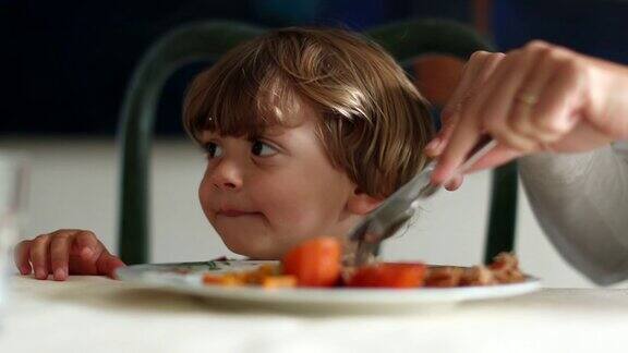小男孩在饭桌上父母在给蹒跚学步的儿子喂食