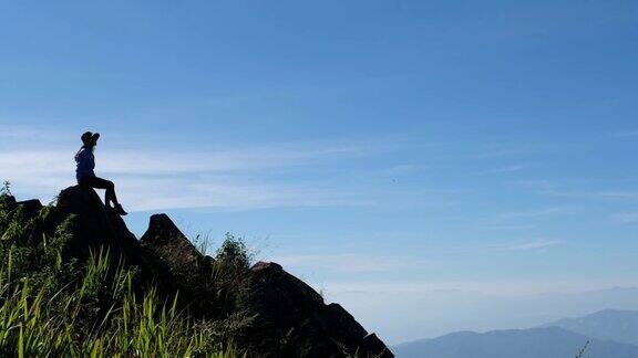 一个女旅行者徒步旅行坐在山顶上看美丽的景色