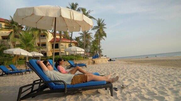快乐的亚洲孩子戴着太阳镜在海滩椅上放松在早上在酒店或度假村度假与家人生活理念