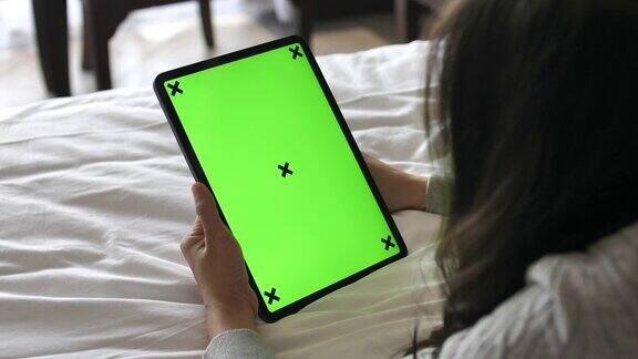 年轻女子躺在床上看数字平板电脑与绿色屏幕在家里垂直