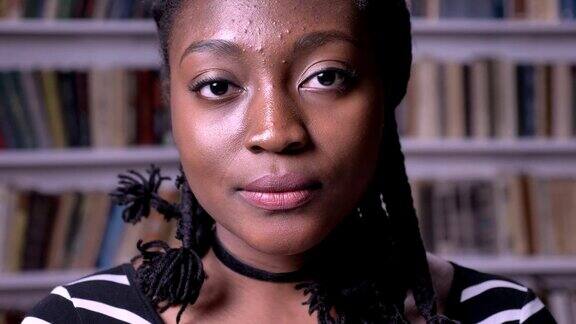 美丽的非裔美国女学生的肖像看着相机和站在图书馆深思和严肃