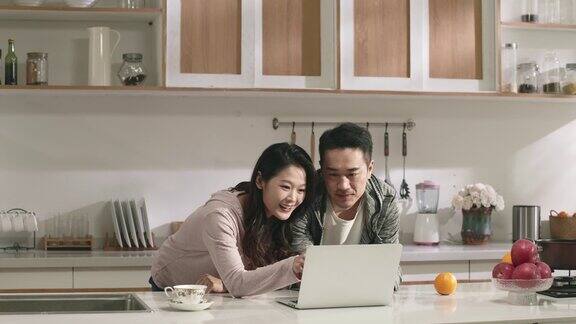 年轻的亚洲夫妇在家里的厨房里一起使用笔记本电脑