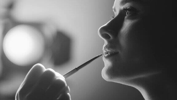 女演员的脸部特写化妆师用化妆刷在嘴唇上涂口红黑白视频
