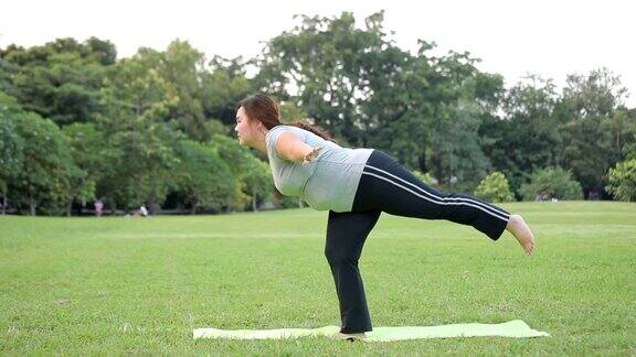 在公园的草地上练习瑜伽的大号亚洲女人