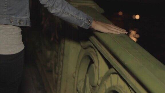 巴黎夜晚一个女人的手在一座桥的栏杆上缓慢移动悲伤的女孩走在后面特写镜头滑动性感动人模糊的彩灯以城市为背景