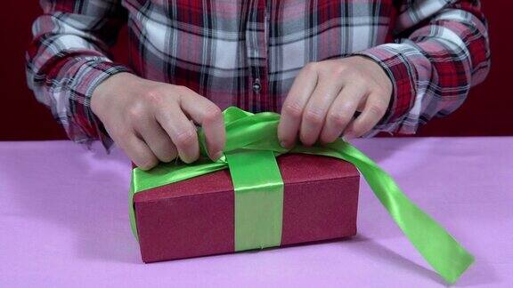 女人用红色包装纸包裹圣诞、新年礼物并系紧绿色丝带蝴蝶结