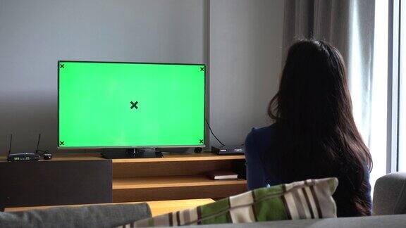 亚洲女人坐在沙发上看电视与色度键在家里