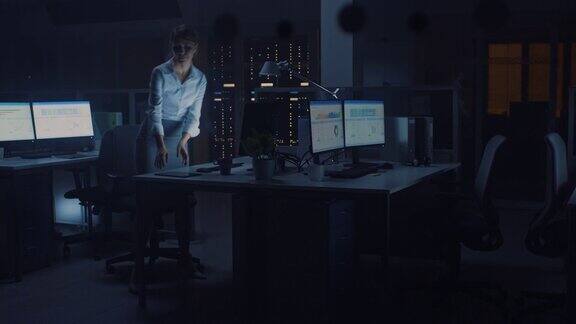 在办公室工作到深夜:女商人使用台式电脑分析使用文件解决问题完成项目后她站起来关了灯离开了