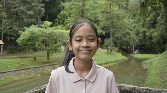 肖像亚洲可爱的女孩是微笑而站在水坝上面的运河在森林公园