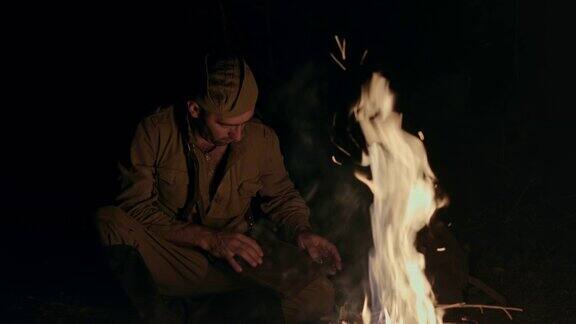 身着制服的士兵晚上蹲在地上用一根棍子点燃熊熊的篝火然后借着火光打开工具箱