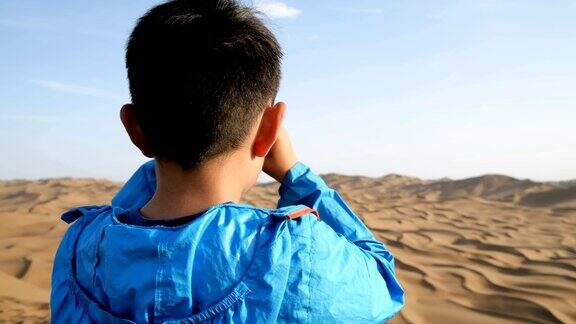 一个小男孩在沙漠里用望远镜看