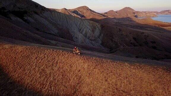 空中拍摄从飞行的无人机一对年轻的游客正在享受美丽的海景日落慢动作而乘坐的ATV运输一对夫妇在海边的小山上骑着四轮自行车4k