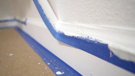 从模塑上去掉遮蔽胶带一个油漆工从墙上扯下蓝色的油漆工胶带露出一块干净的边踢脚板