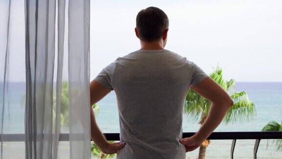度假的男人拉开窗帘走到阳台上从阳台上欣赏地中海的海景