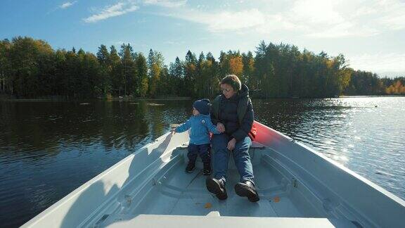 母亲和儿子坐在小船上在森林附近的湖上漂流