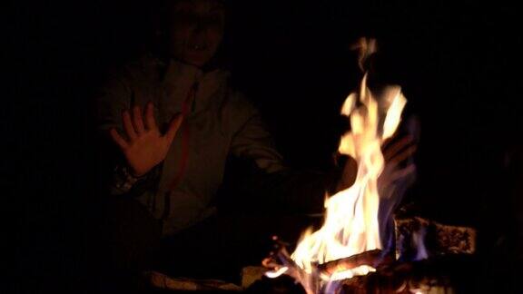 在森林露营时女孩在篝火旁暖手