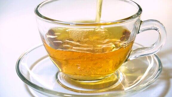 将香喷喷的红茶从茶壶中倒进白色背景上的透明玻璃茶杯中