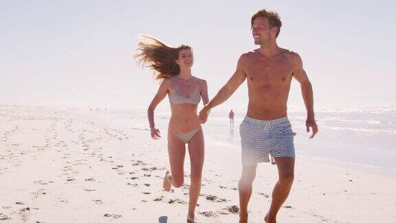 穿着泳衣的情侣一起在夏天的海滩上跑步