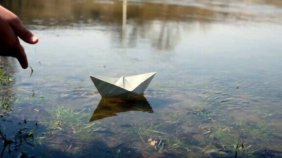 孩子在池塘边拿着一只纸船