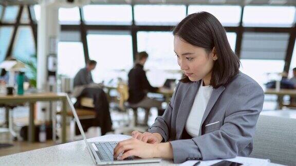 年轻的亚洲女商务经理使用笔记本电脑在大的现代办公室工作