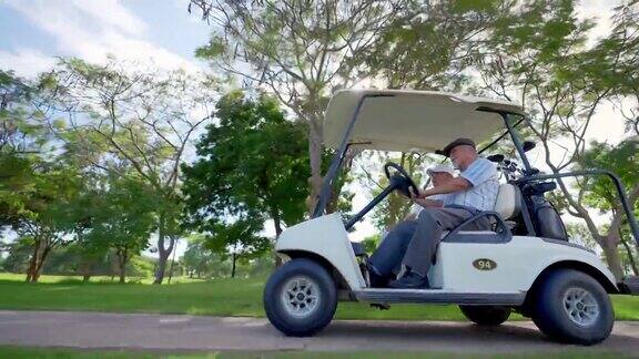 在夏日阳光明媚的高尔夫球场上驾驶高尔夫球车的亚洲老人的4K集团