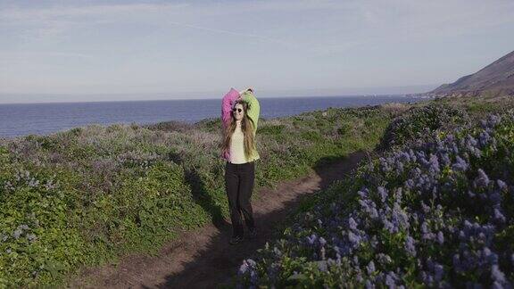 一名背着背包的女子走在加州大苏尔海岸的开花草地上