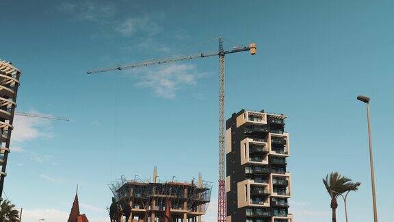 在蓝天的衬托下建筑工人和高塔起重机在工地上工作的时间流逝建设现代住宅公寓楼起重机在工地上装载重型材料