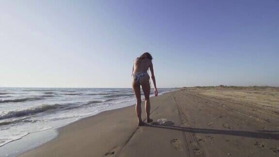 美丽的女孩走在沙滩上捡垃圾污染