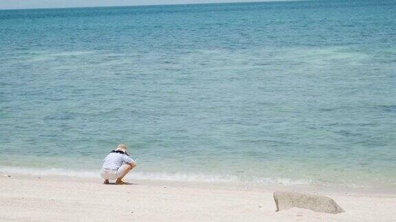 快乐的肖像女人旅行者与帽子独自坐在沙滩溅水