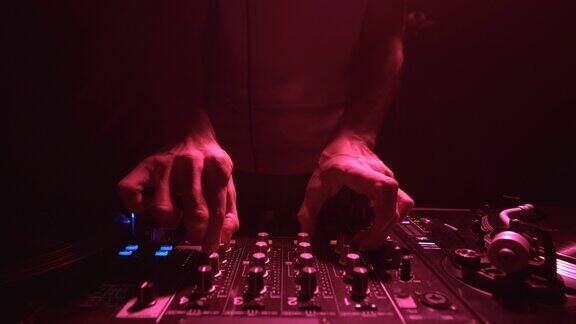 俱乐部DJ的手在红色的舞台灯光下混合音乐音乐节目主持人使用混音器在电子音乐派对上混音黑胶唱片