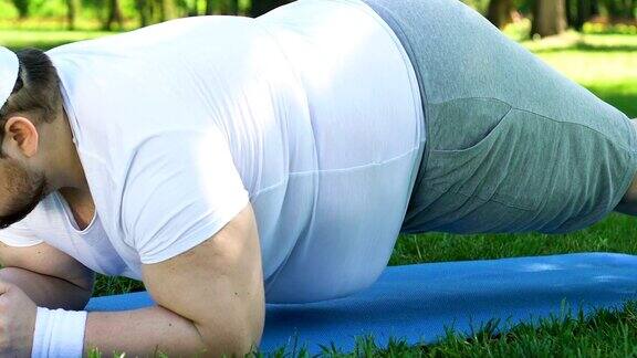 加号男子在公园的垫子上做平板支撑试图减肥肥胖