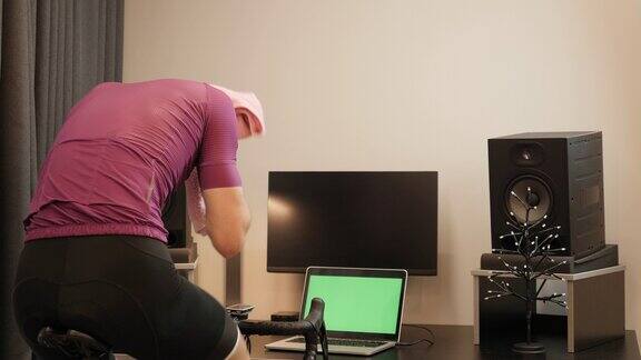 职业自行车手正在自行车智能教练上做间歇训练男人正在家用健身自行车训练器上骑车室内循环在线健身锻炼