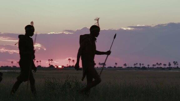 在博茨瓦纳的Makgadikgadi草原上夕阳西下三名桑族人丛林人穿着传统服饰走过摄像机的4K侧面画面