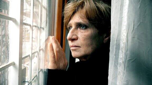 悲伤和体贴成熟的女人看着窗外落地窗肖像