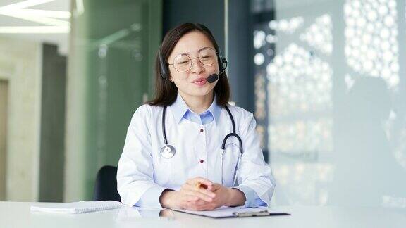摄像头的观点亚洲女医生在医院诊所用无线耳机进行视频通话